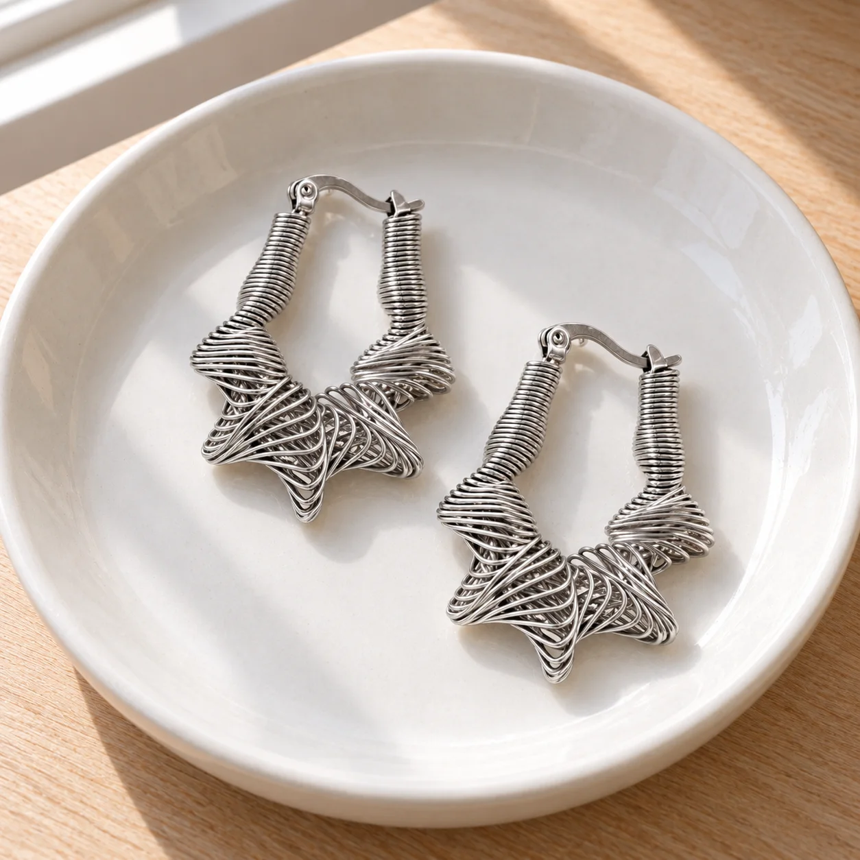 Nina Woven Star Hoops resting flat in a shallow white ceramic bowl